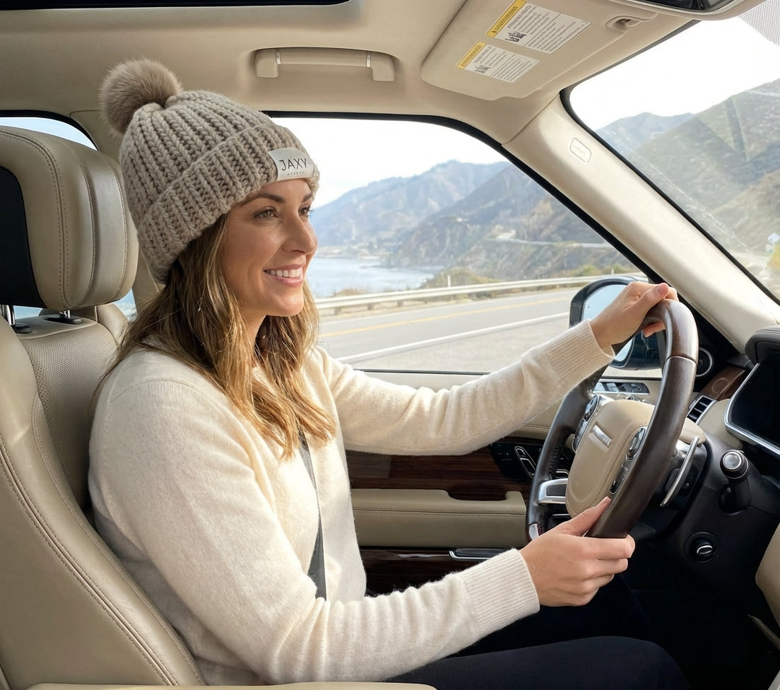 Woman driving a car wearing jaxy beanie in (sandstone) with mountains in the background
