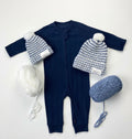 Navy baby onesie with two sky jaxy beanies and two balls of yarn on a white background