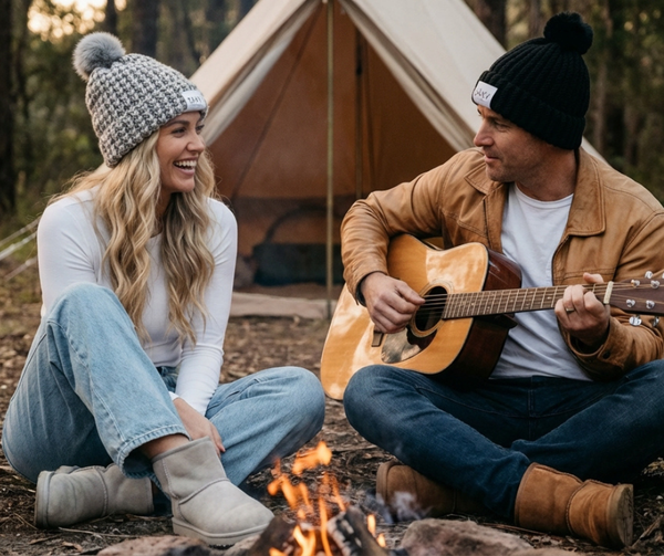 Two people sitting by a campfire with a tent in the background
