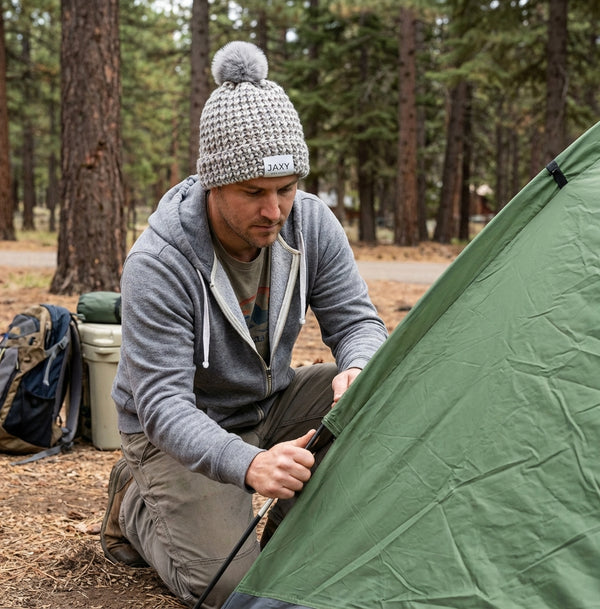 Man wearing marble-grey jaxy beanie setting up a green tent in a forest